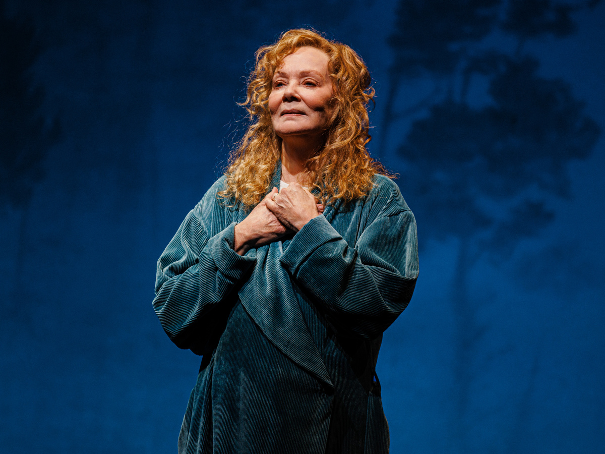 Jean Smart as Izzy stands with her hands clasped to her chest